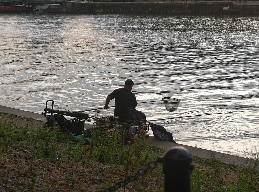 An angler casting from a dark shoreline under a headlamp glow at dusk